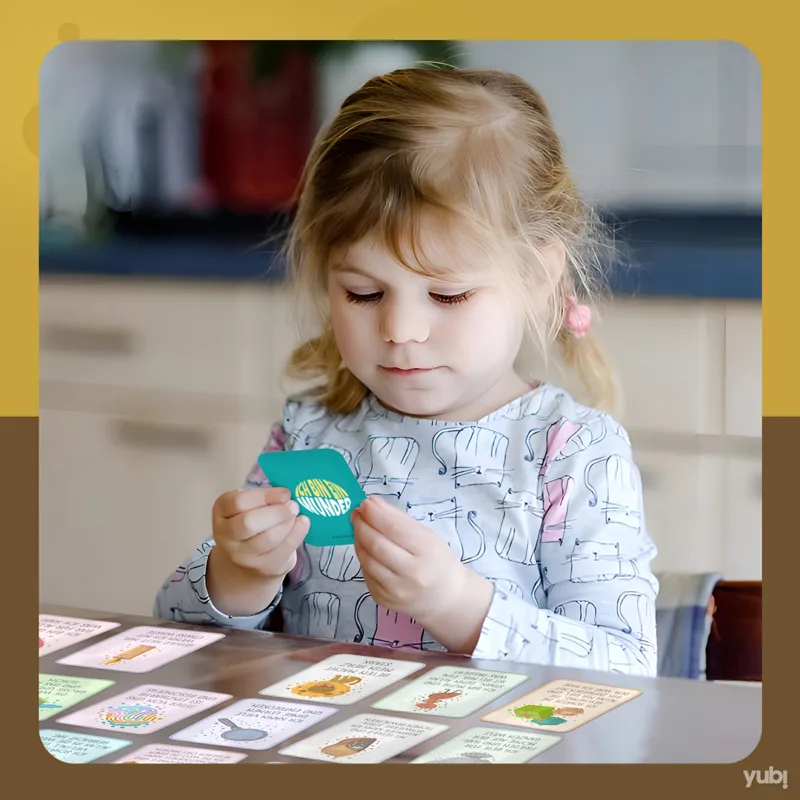 Konzentriertes kleines Mädchen, das eine Spielkarte betrachtet, mit mehreren Karten auf dem Tisch vor ihr.